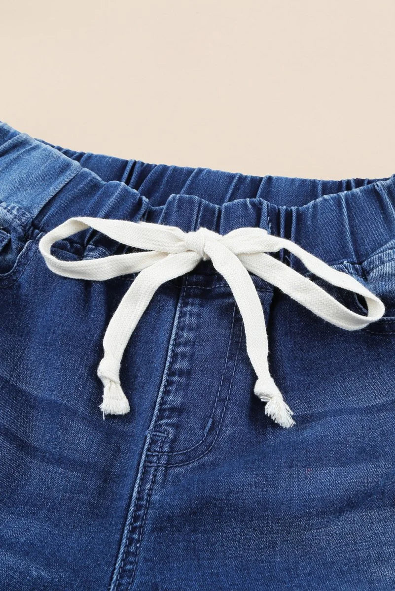 Close-up of dark blue denim pants with a white drawstring bow and elastic waistband.