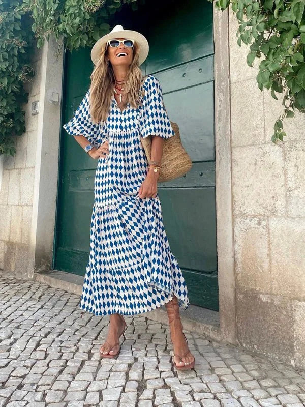 Woman in a blue and white geometric print tiered maxi dress, white hat, and brown sandals.
