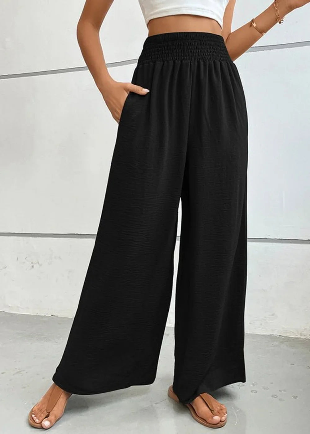 Black high-waisted wide-leg pants with smocked waist and textured fabric, shown on a model.