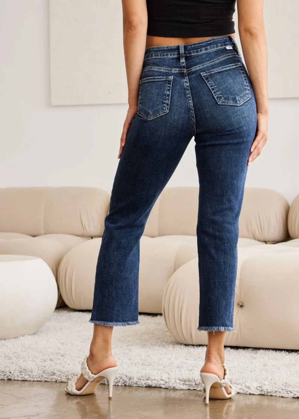 Back view of dark wash denim jeans with a frayed hem and regular fit, worn by a model.