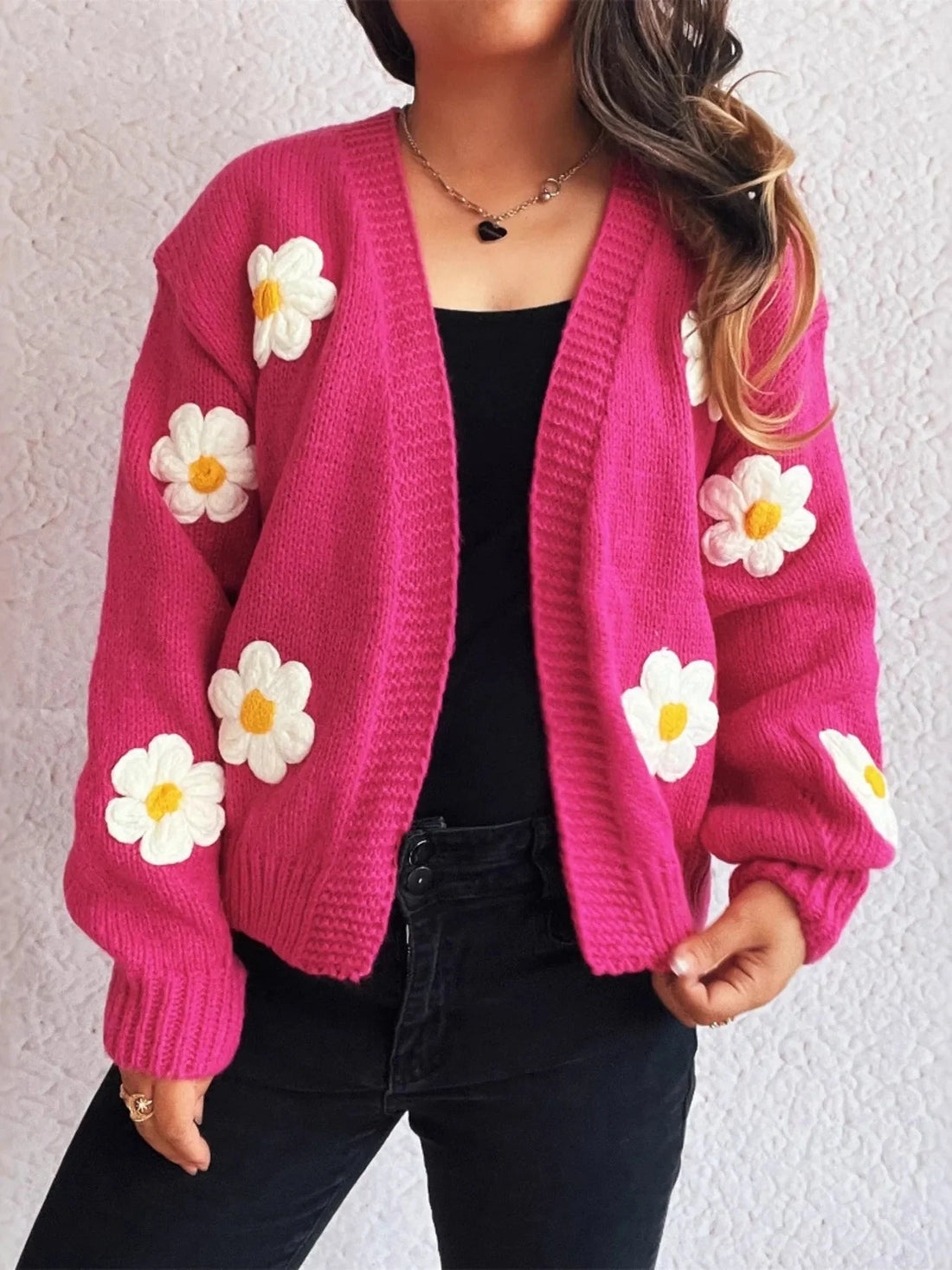 Hot pink knit cardigan with white and yellow daisy appliques, worn by a model.