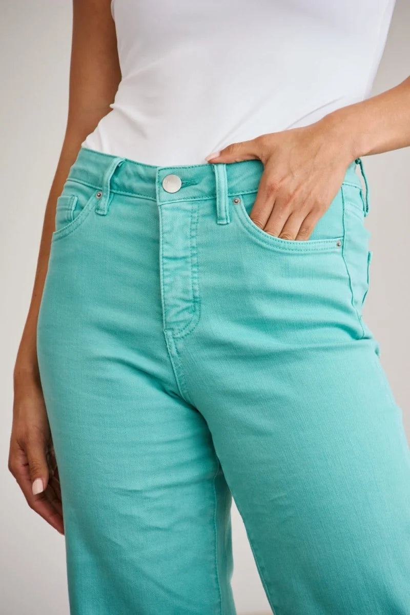 Close-up of turquoise denim jeans with a button closure, pockets, and moderate stretch on a model.