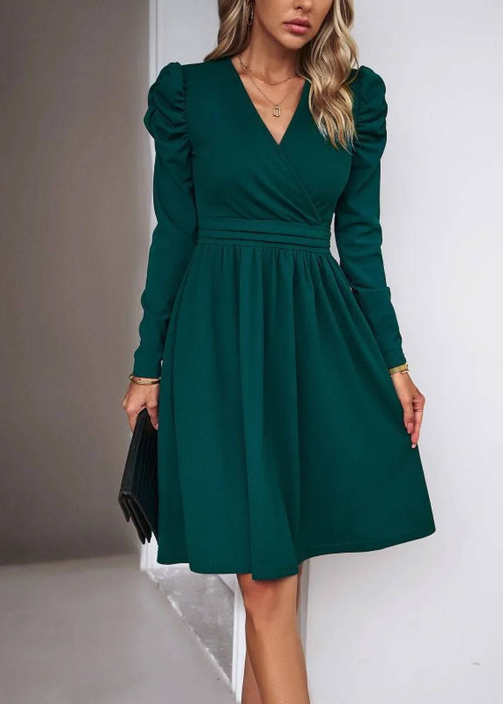 Emerald green faux wrap dress with ruched puff sleeves and a pleated skirt, held with a clutch.