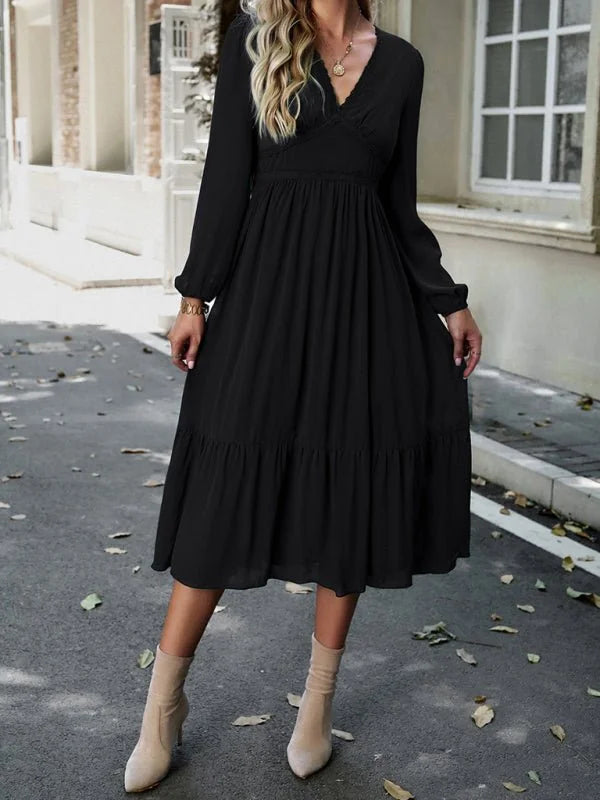 Black midi dress with v-neck, tiered skirt, and long sleeves, worn with ankle boots.