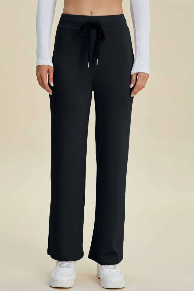 Black, wide-leg, high-waisted knit pants with drawstring closure and white sneakers.