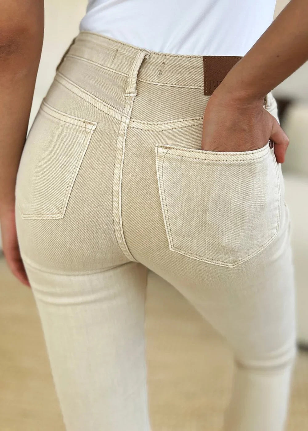 Close-up of light beige denim jeans showing back pockets and a leather patch.
