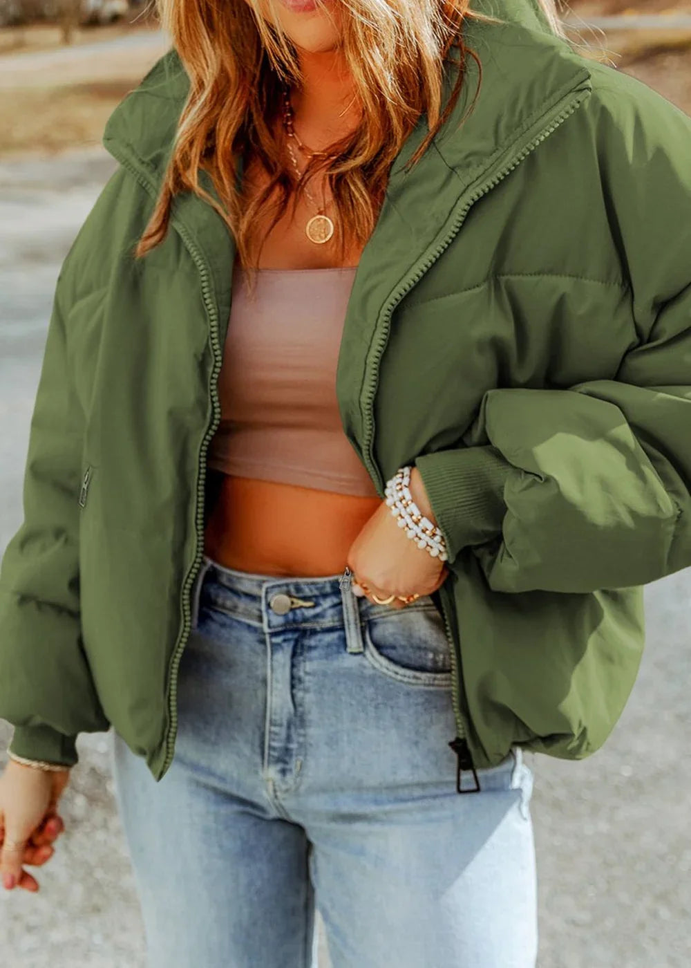 Olive green puffer jacket with zipper closure, worn with light wash jeans and a tan top.