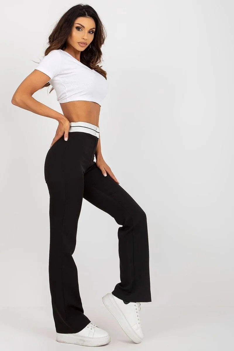 Black, high-waisted, wide-leg pants with a white waistband detail, worn by a model with white sneakers.