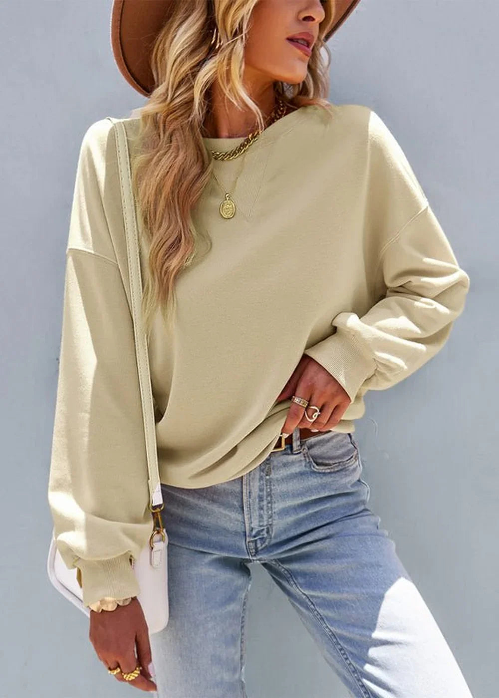 Model in loose-fit, cream-colored crewneck sweatshirt and light wash jeans.