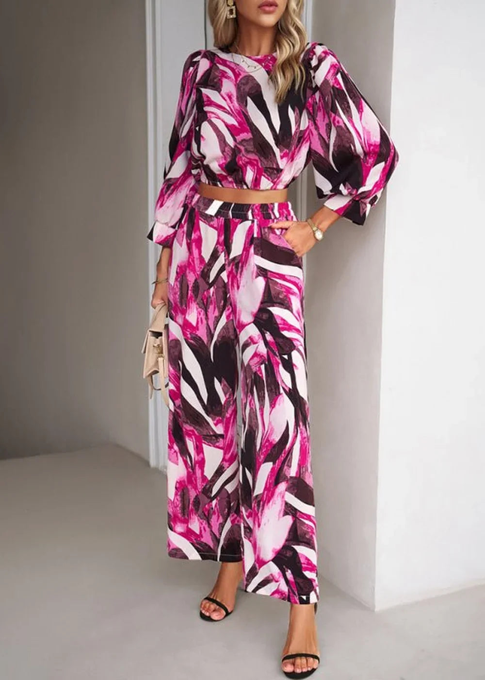 Woman in a vibrant pink, white, and black abstract print two-piece set, featuring a cropped long-sleeve top and wide-leg p...