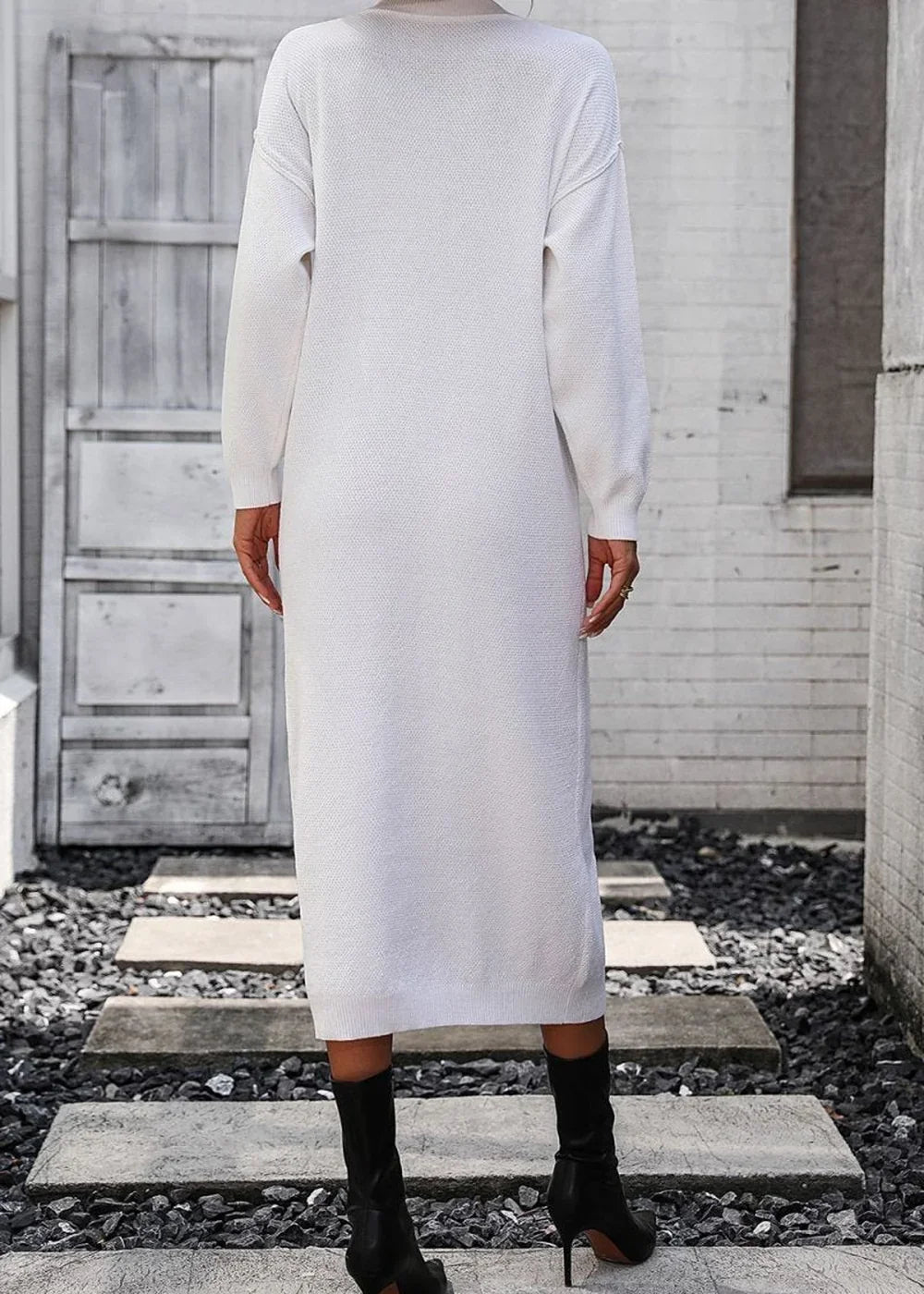 Back view of a white, long-sleeved, midi-length knit sweater dress on a model wearing black heeled boots.
