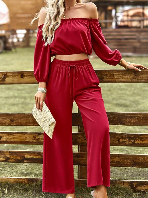 Red off-the-shoulder crop top and wide-leg pants set with a straw clutch.