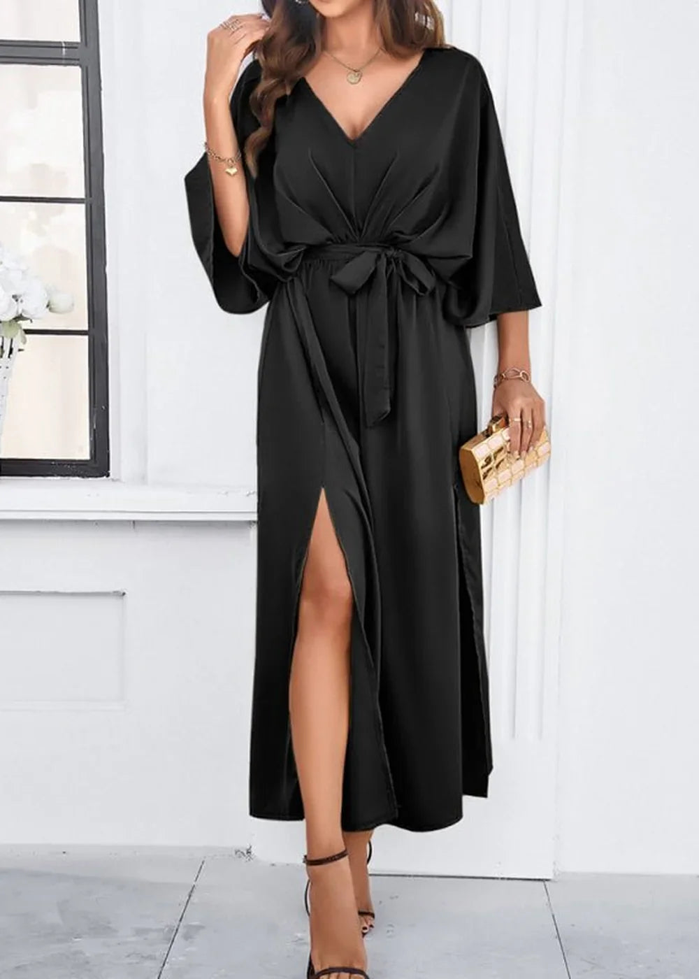 Sleek black satin maxi dress with a V-neck, tie waist, and thigh-high slits, worn with gold accessories.