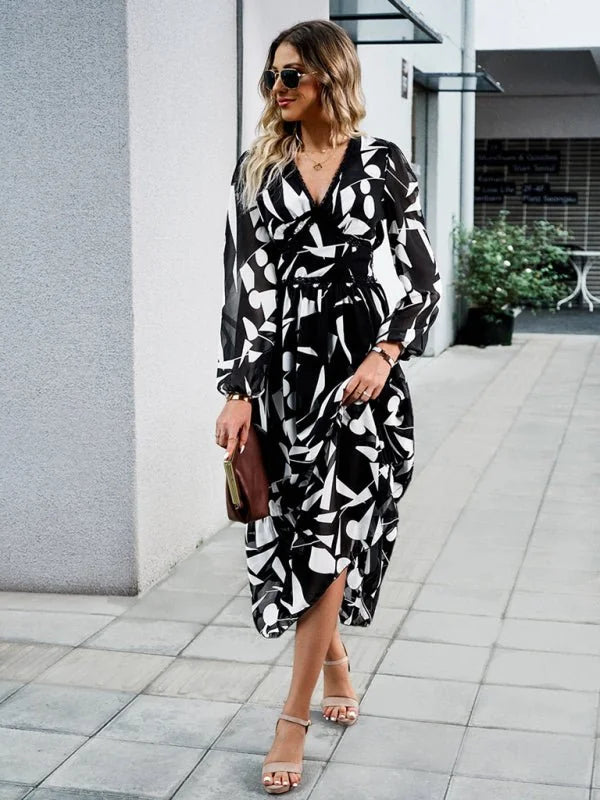 Woman in a black and white abstract print midi dress with V-neck and long sleeves, holding a brown clutch.