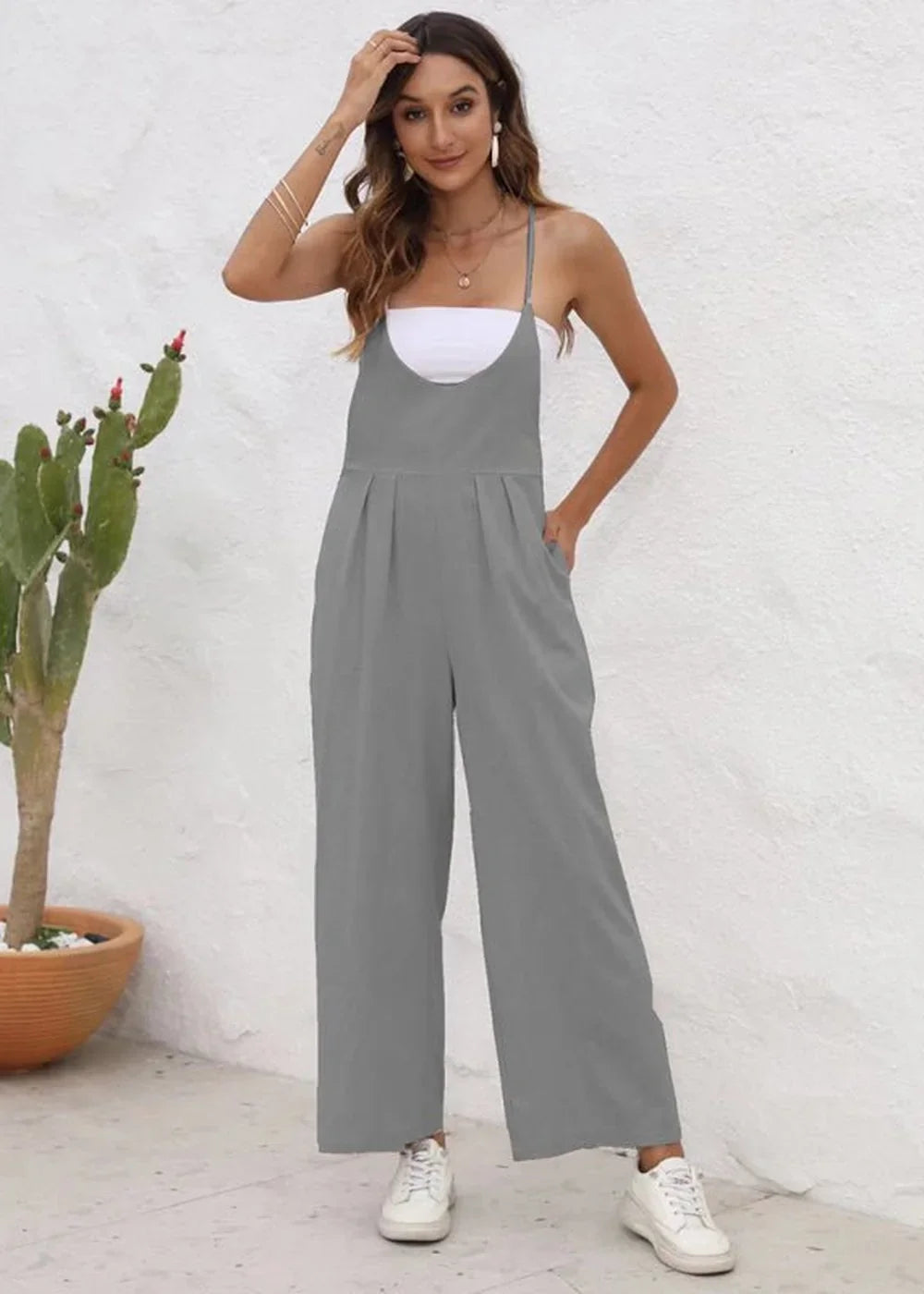 Full-length grey polyester jumpsuit with spaghetti straps, a white undershirt, and white sneakers, on model.
