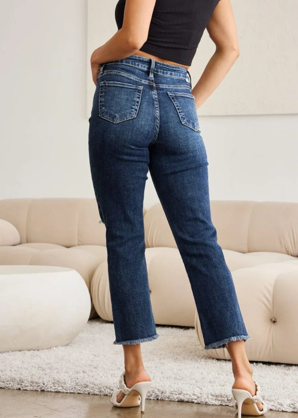 Dark wash denim jeans with frayed hem and distressed detail, on model.