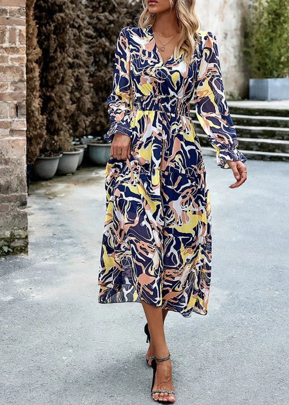 A woman models a flowy, midi-length dress with a vibrant abstract print in navy, yellow, and coral.