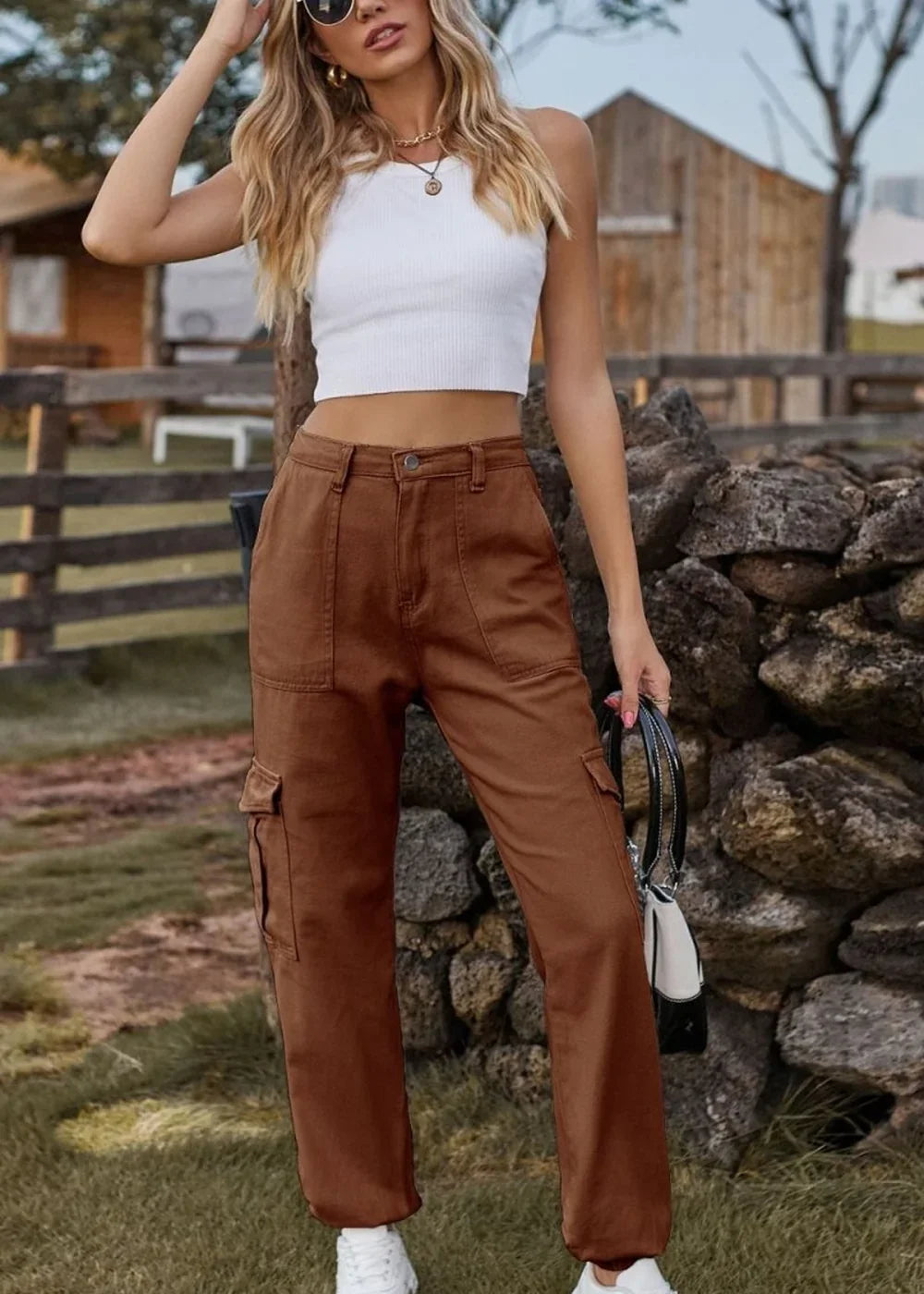 A woman wearing brown cargo pants and a white crop top, holding a black and white purse.