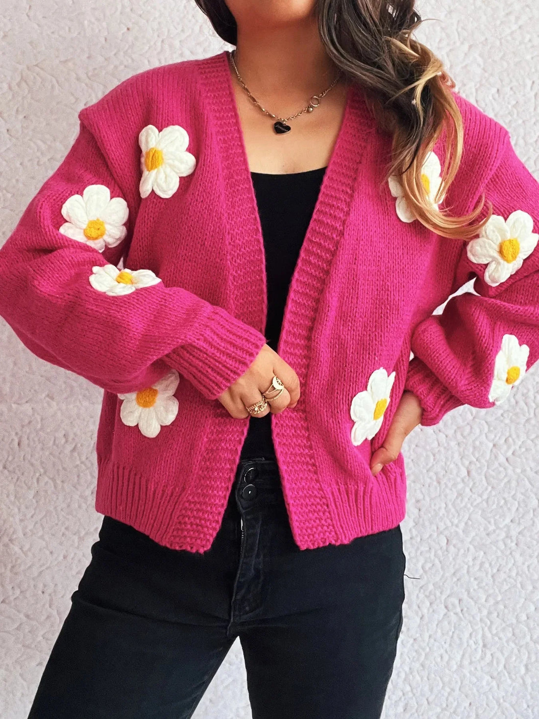 Pink knit cardigan with white floral appliques and yellow centers, worn by a model over a black top.