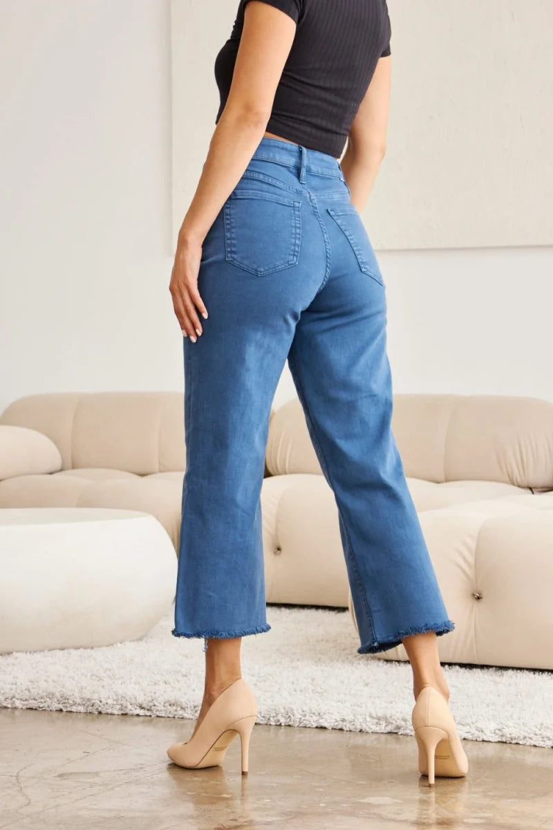 Blue denim crop pants with frayed hem, shown from the back on a model wearing nude heels.