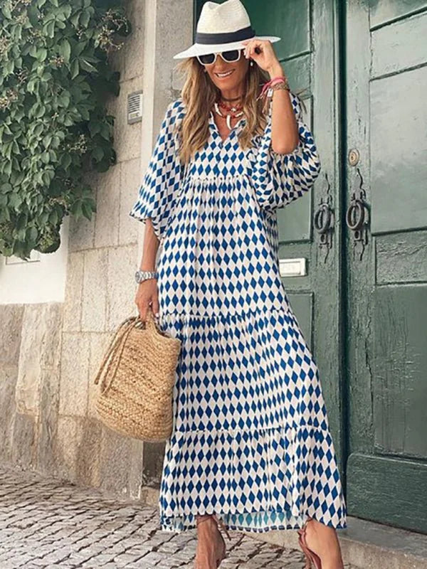 Woman in a blue and white diamond print tiered maxi dress, straw hat, and woven bag.