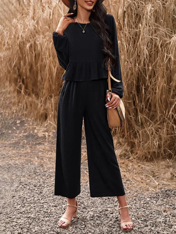 Black wide-leg jumpsuit with peplum top and tan sandals on model.