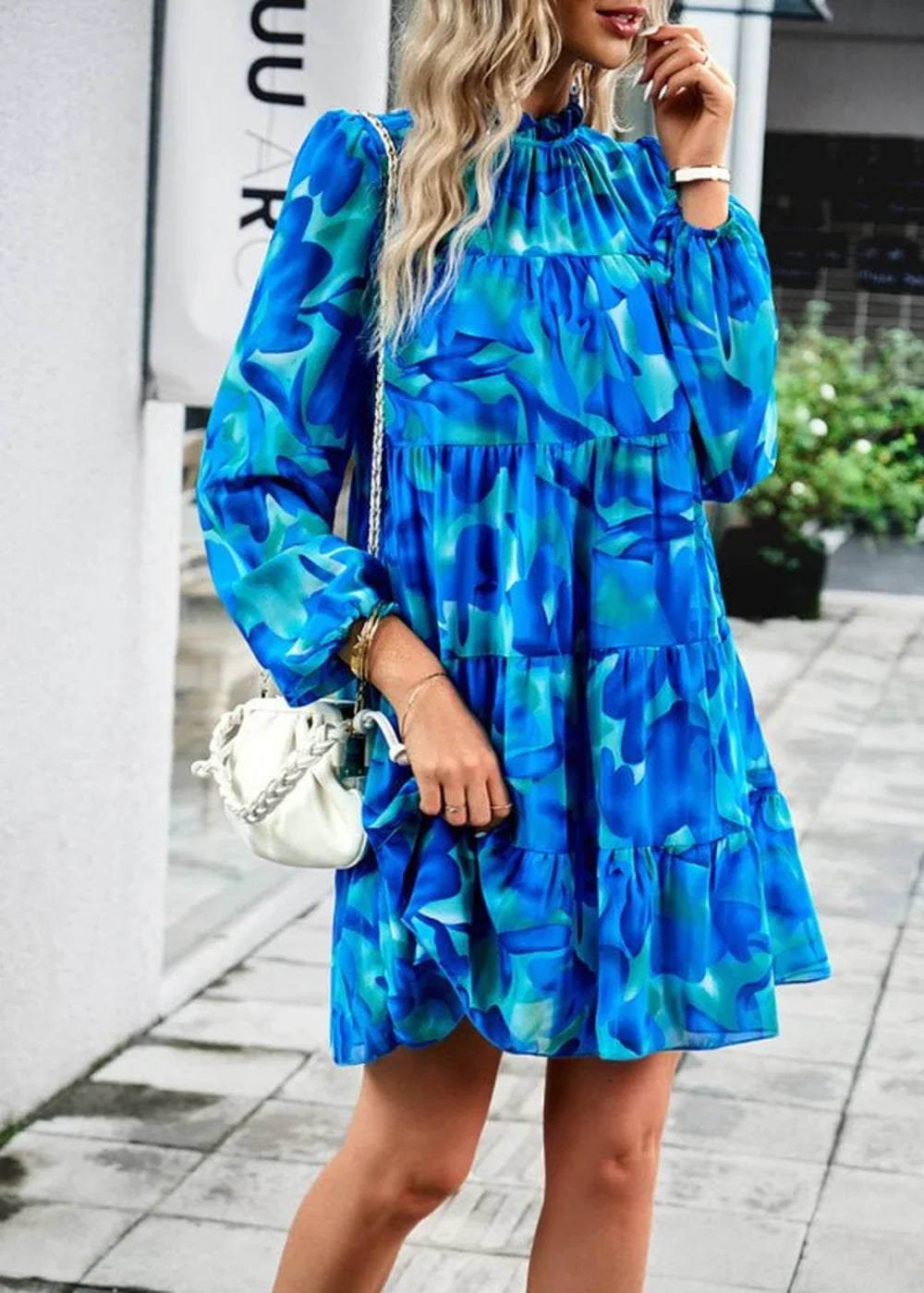 Blue and teal floral print tiered mini dress with long sleeves and a white crossbody bag.