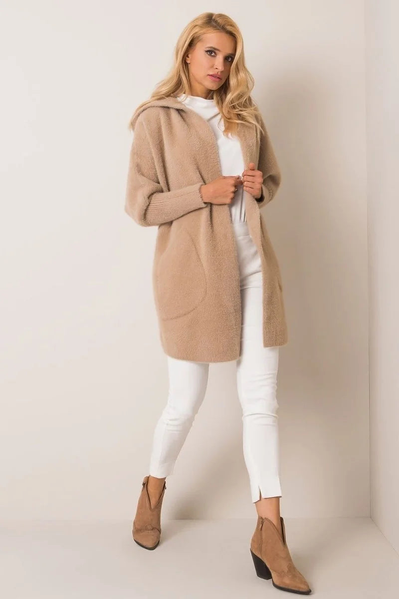 Woman wearing a fuzzy beige hooded cardigan over white pants and tan ankle boots.
