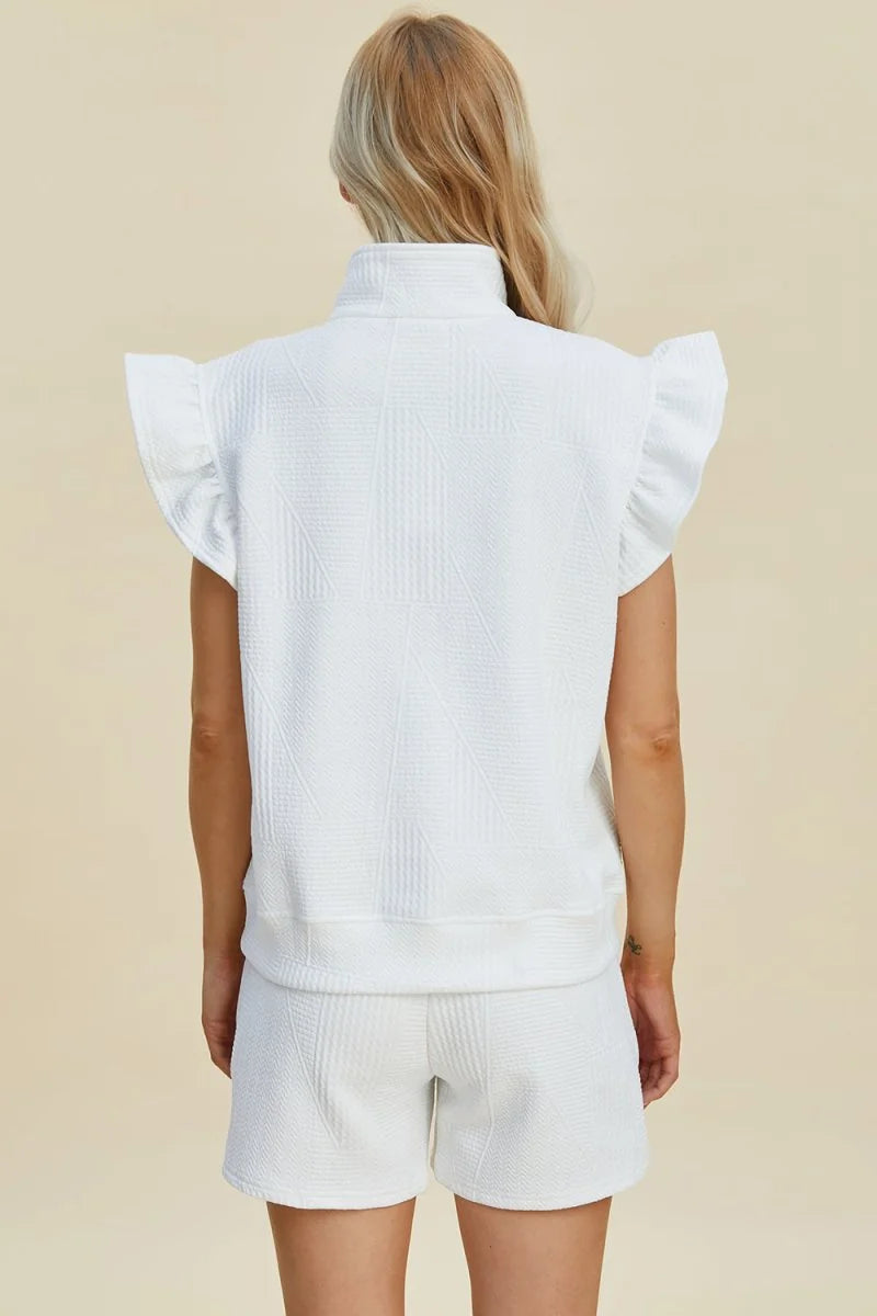 White textured shorts and sleeveless top with ruffled shoulders on a model.