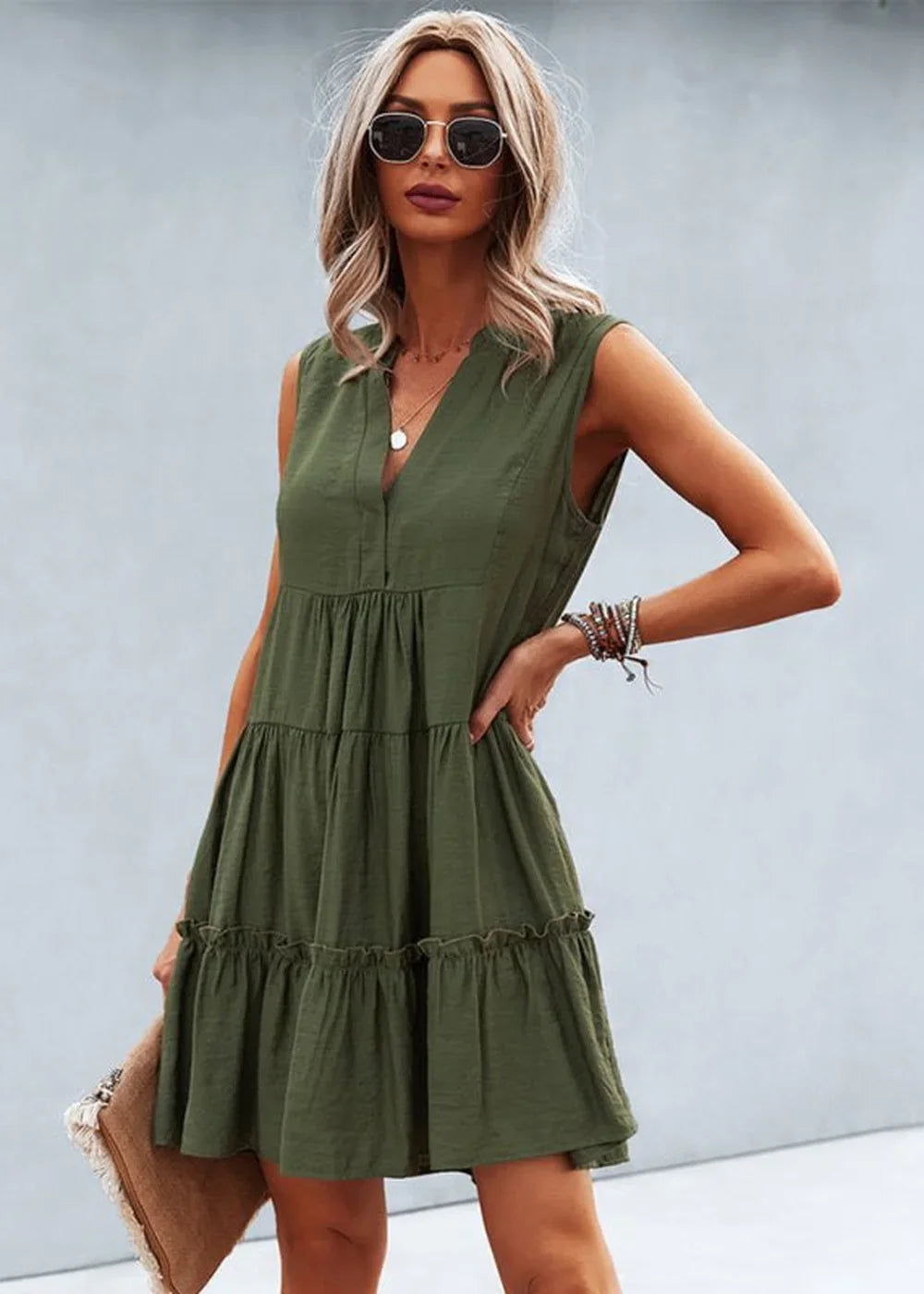 Olive green tiered v-neck sleeveless dress with ruffled hem, worn by a model with sunglasses and a clutch.