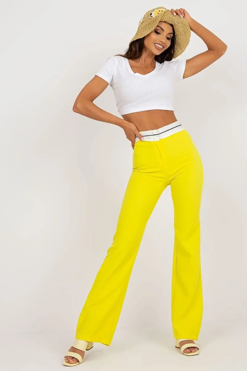 Woman in bright yellow flared pants with a white waistband and white heeled sandals.