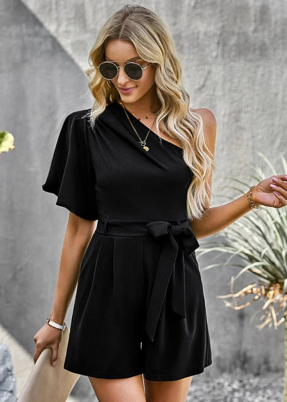 Black one-shoulder romper with flutter sleeve, belted waist, and shorts.