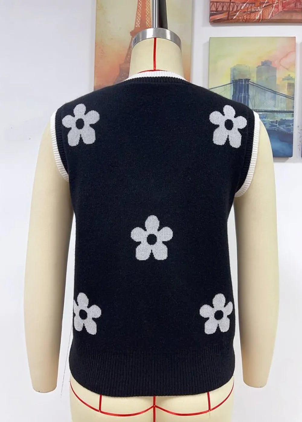 Black knit vest with white floral pattern and contrast trim, shown on mannequin.