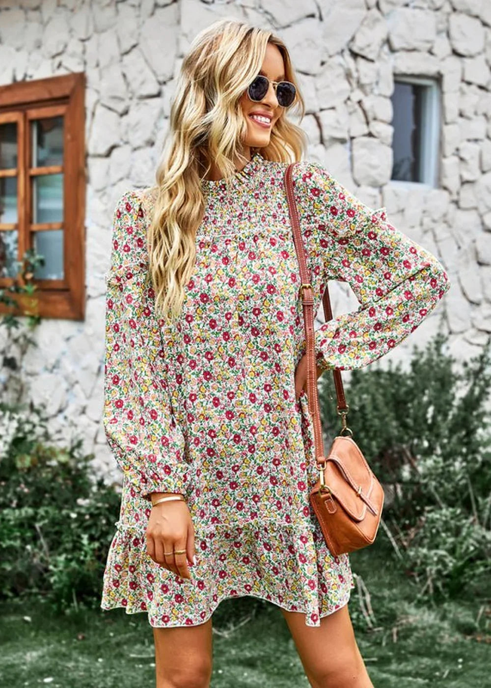 Woman in a long-sleeved floral print dress with smocked neckline and ruffled hem, carrying a brown crossbody bag.