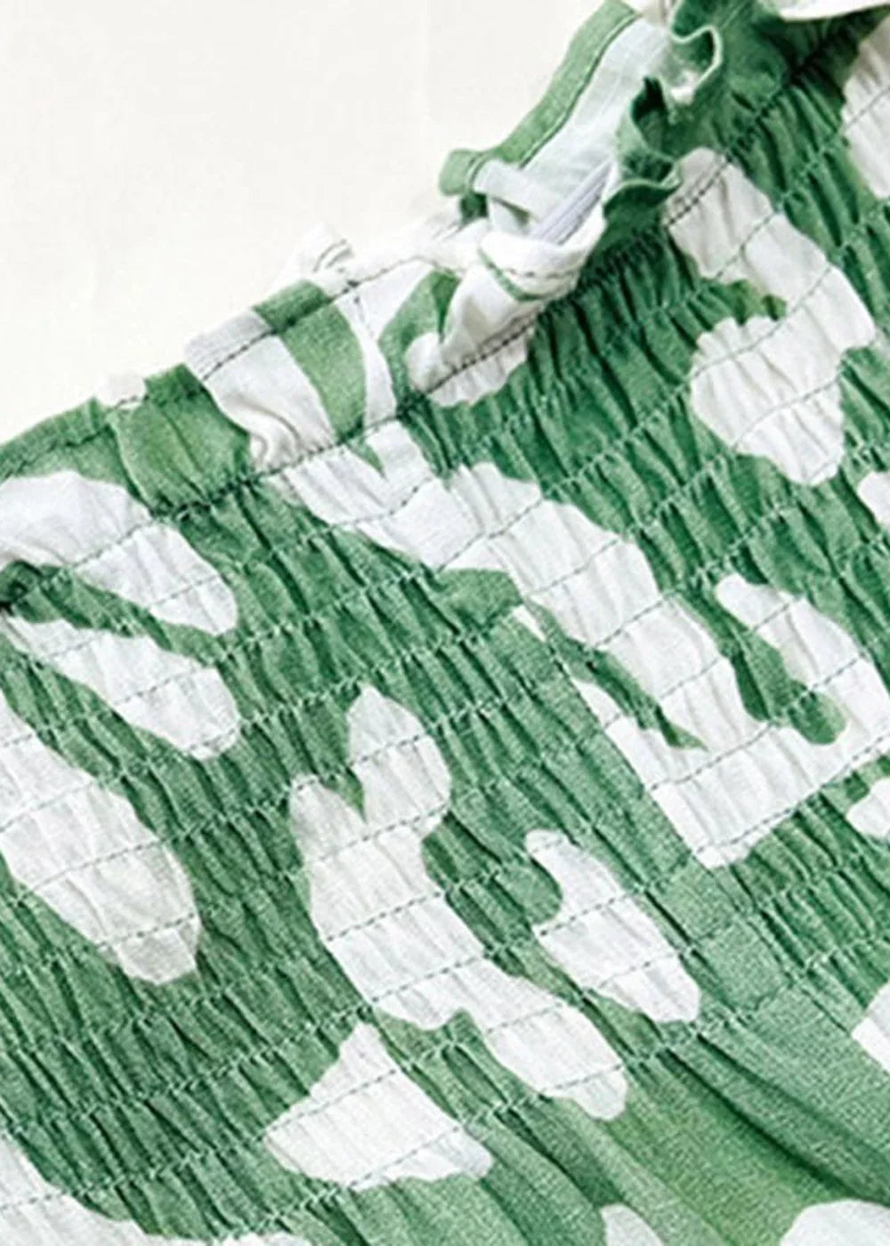 Close-up of green and white abstract print smocked fabric with a zipper detail.