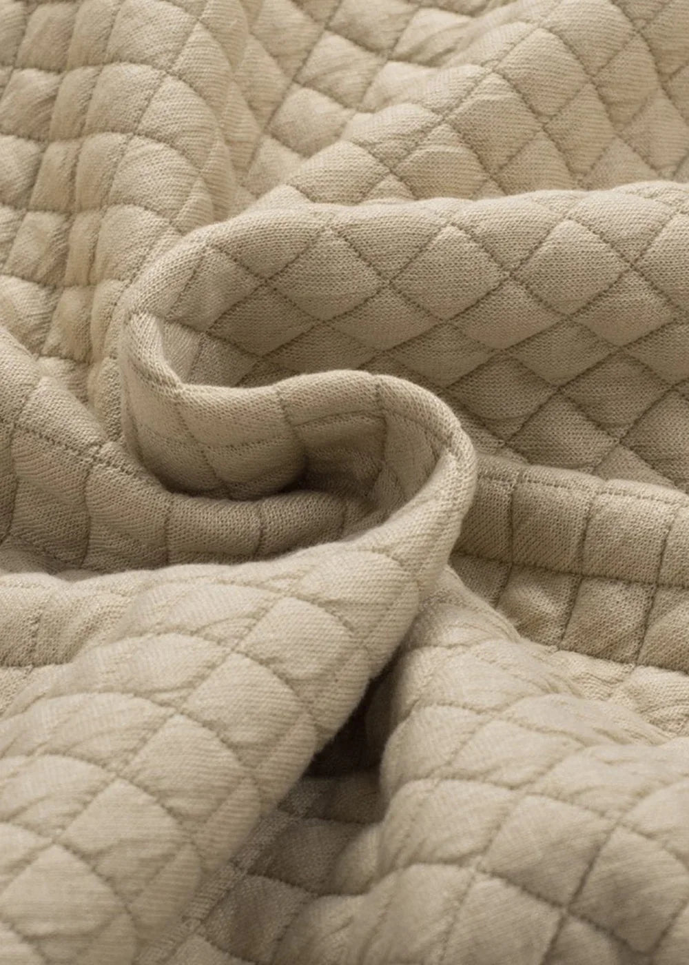 Close-up of soft, beige quilted fabric with a diamond pattern, showing texture and drape.