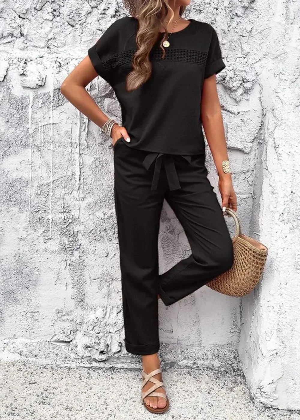 Black linen-blend pantsuit with tie waist, short sleeves, and woven straw bag.