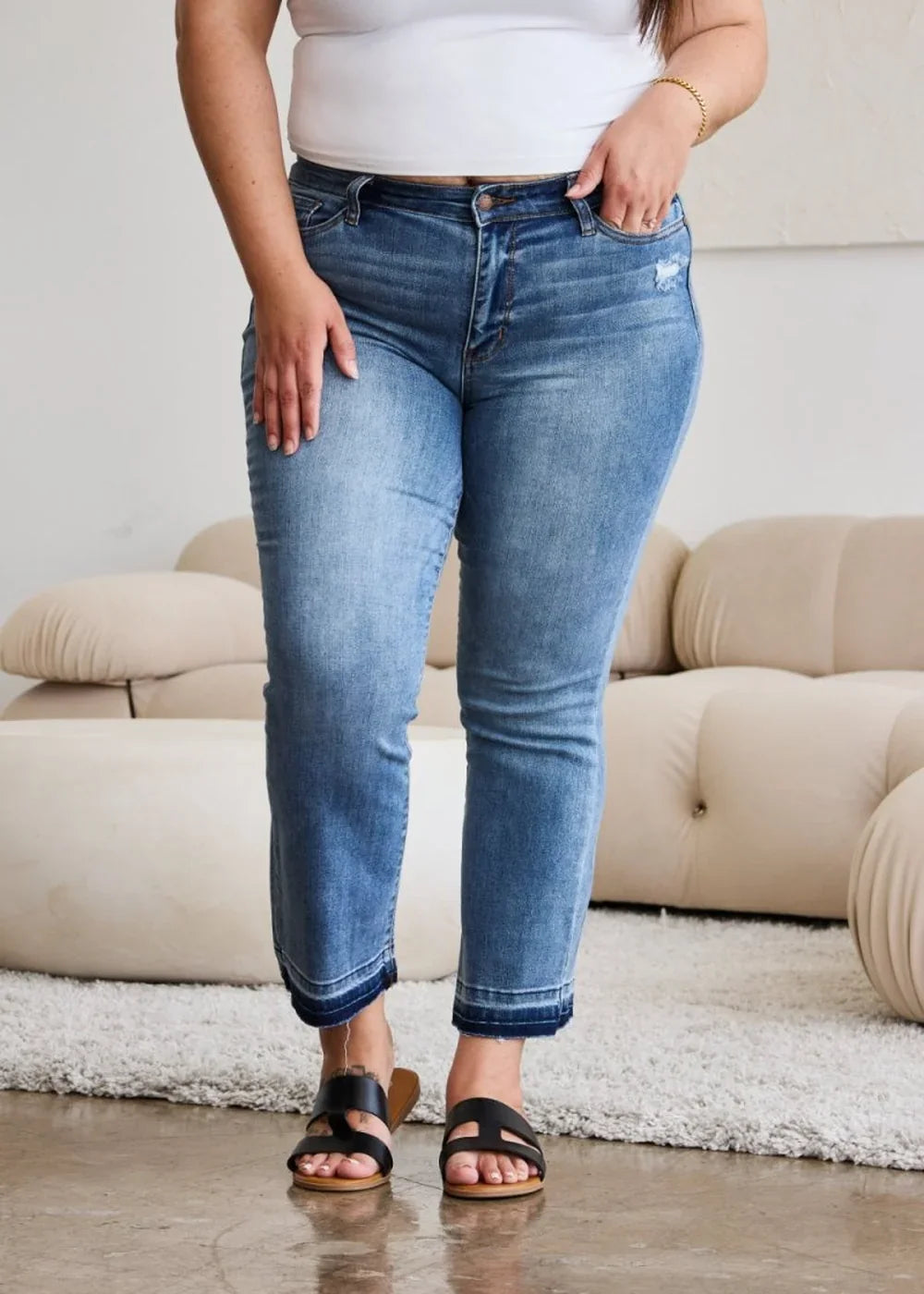 Medium wash distressed denim jeans with a frayed hem, worn by a model.