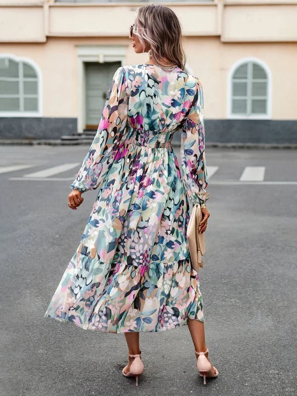 Woman in a flowing, multi-colored floral print midi dress with long sleeves and a cinched waist.