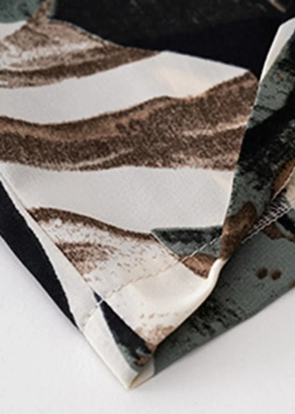 Close-up of fabric with a abstract print in shades of white, brown, and dark green, showing seam detail.