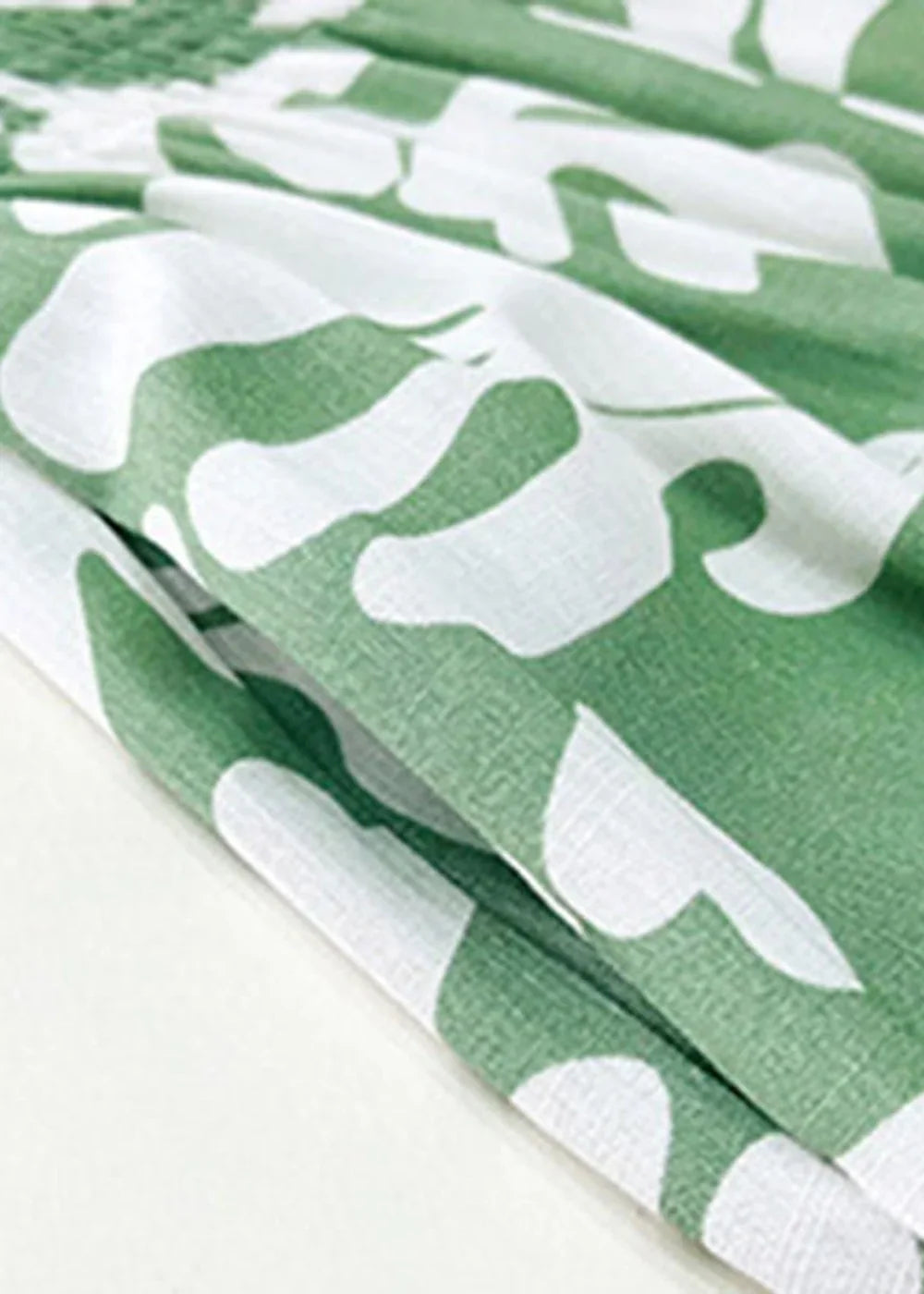 Close-up of green and white leaf print viscose fabric with soft folds.