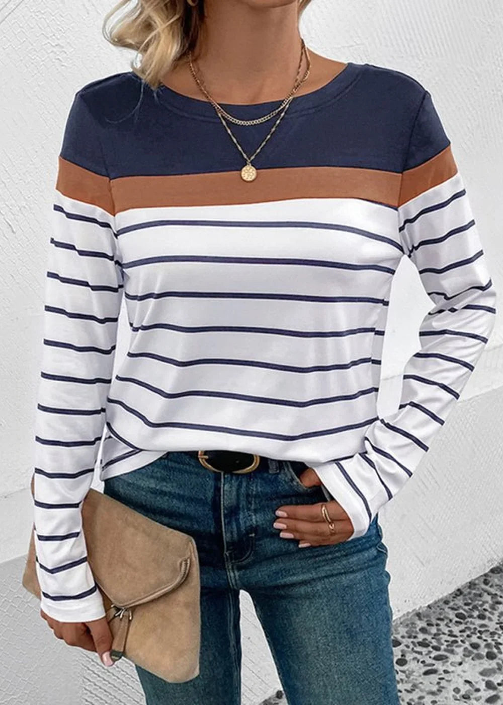 Long-sleeved striped top with navy, brown, and white bands, worn by a model with jeans and a clutch.