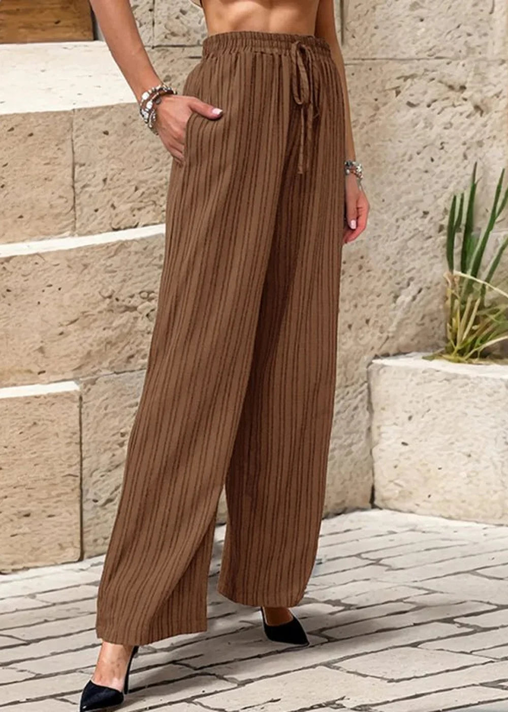 Brown wide-leg pants with a vertical stripe pattern and drawstring waist, shown on a model.