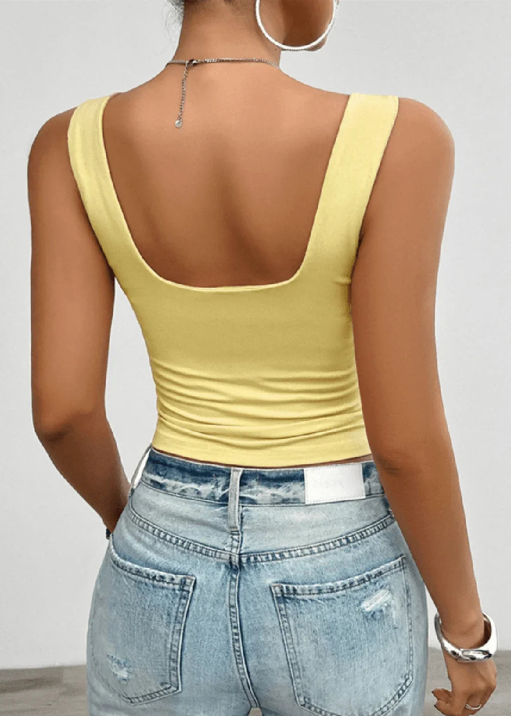 Back view of a slim-fit, pale yellow scoop-neck tank top with distressed light-wash denim jeans.