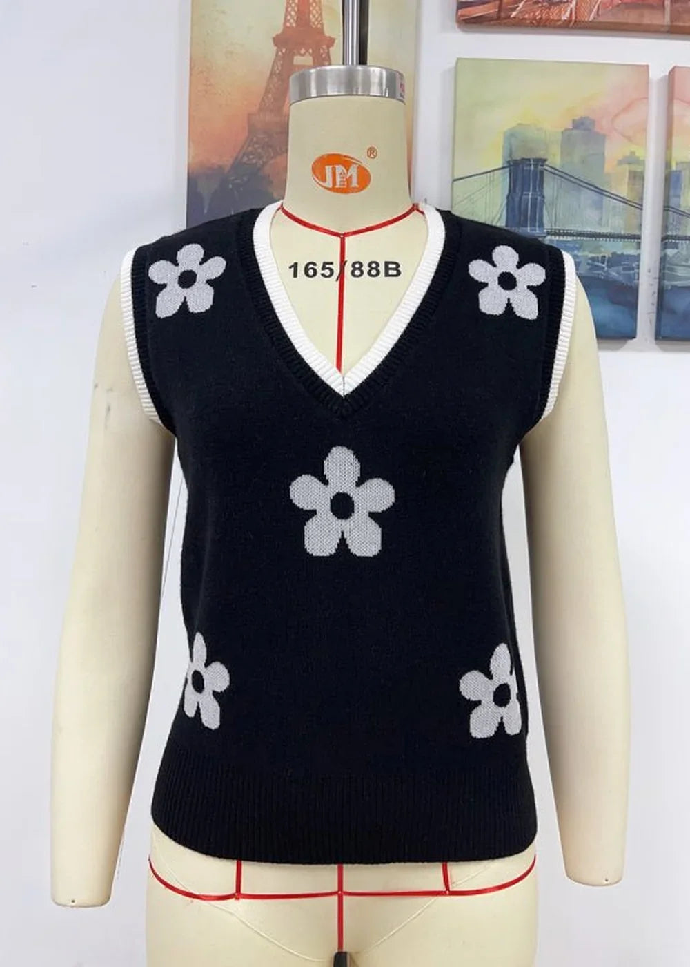 Black V-neck sweater vest with white floral pattern and white trim on model.
