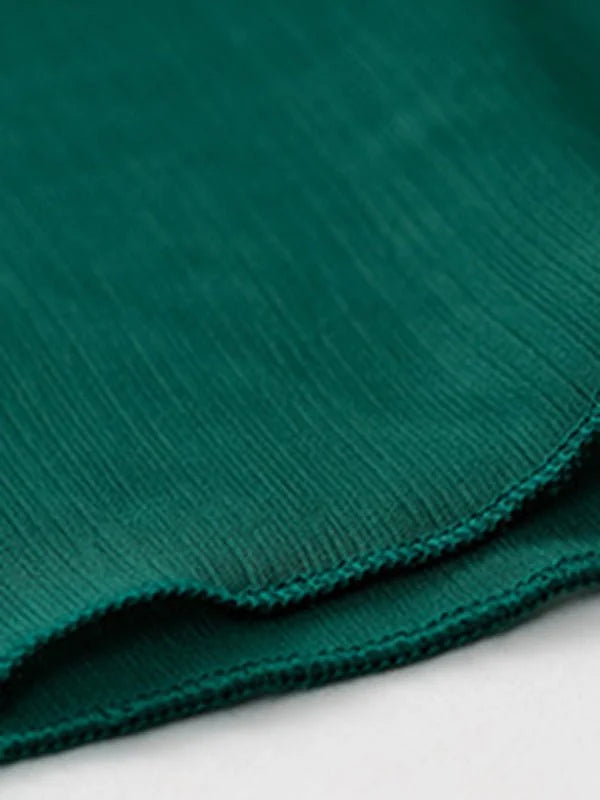 Close-up of emerald green polyester fabric with subtle vertical pleating and a stitched hem.