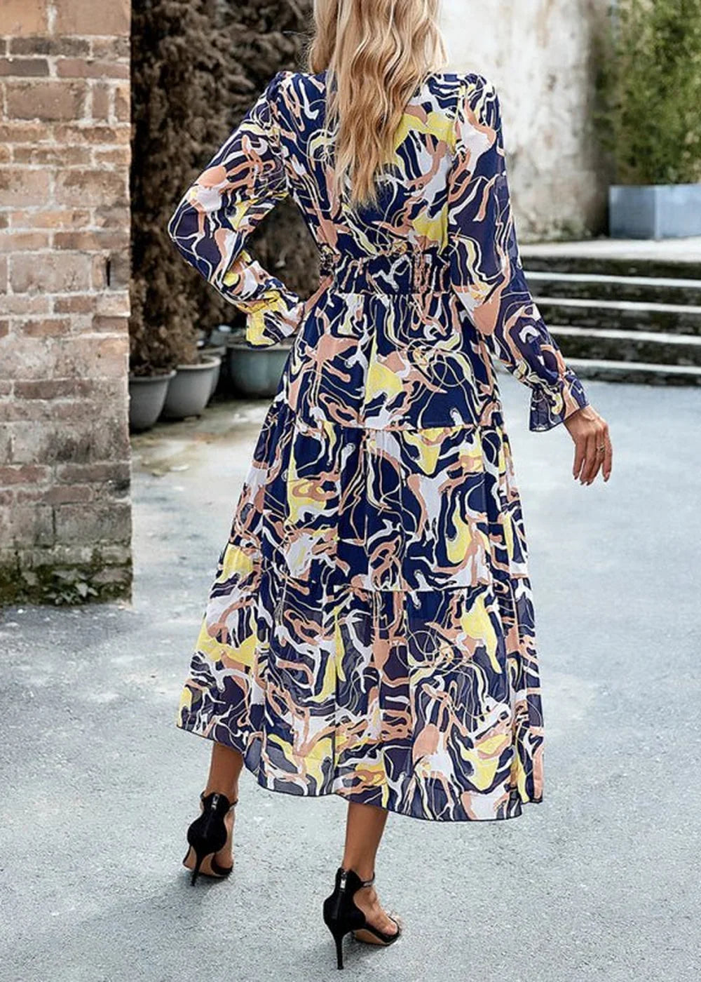 Navy blue dress with a colorful abstract print, long sleeves, and tiered skirt, worn by a model from behind.