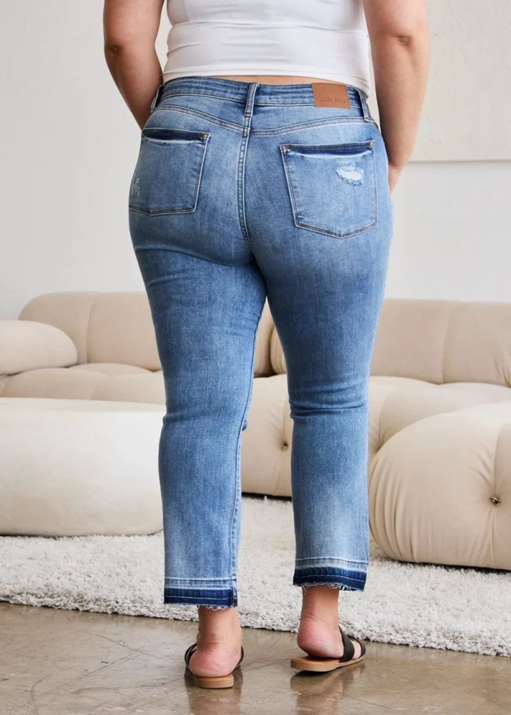 Back view of medium wash distressed denim jeans with frayed hem detail and a regular fit.