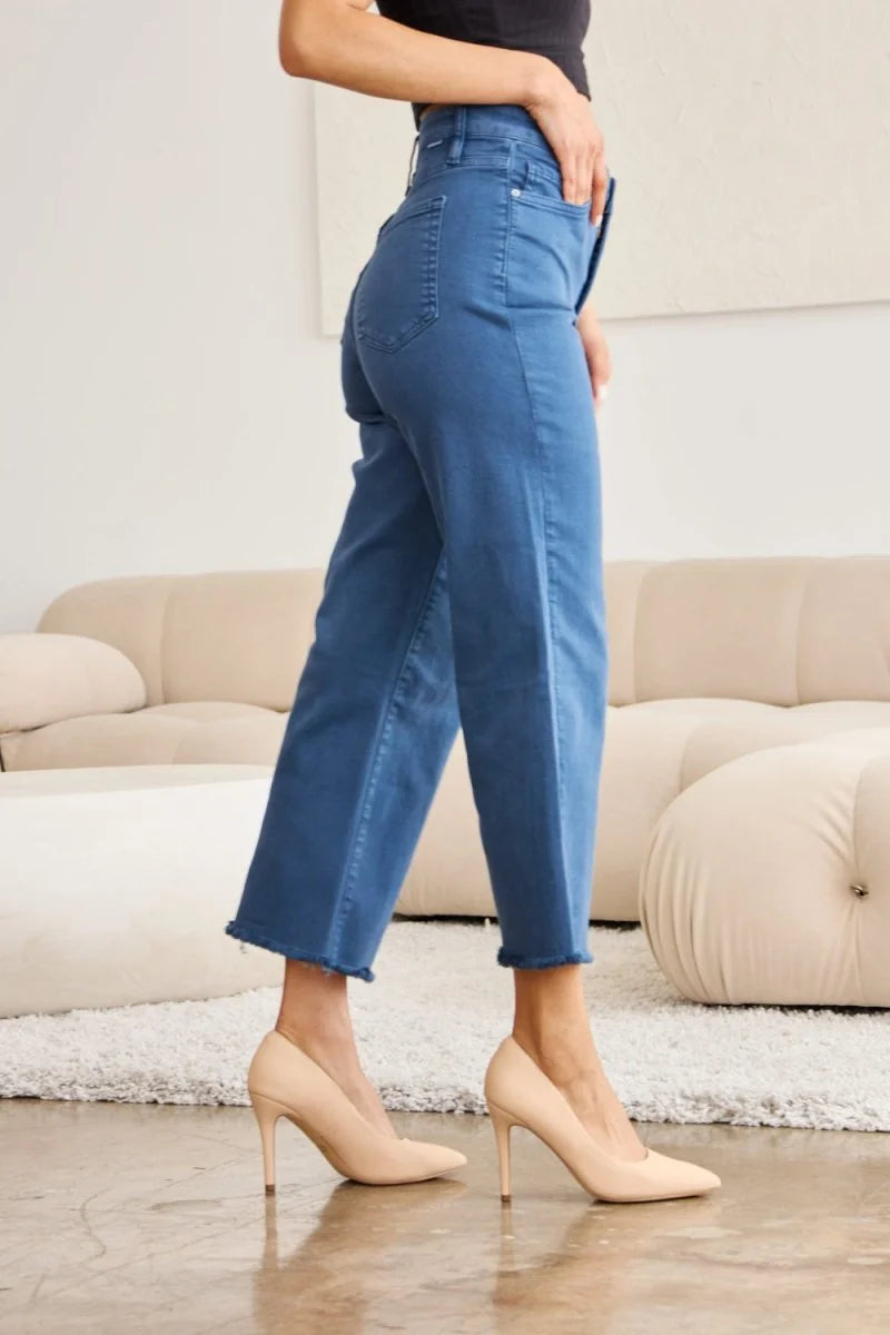 Model wearing cropped, frayed-hem jeans in a medium blue wash, paired with nude heels.