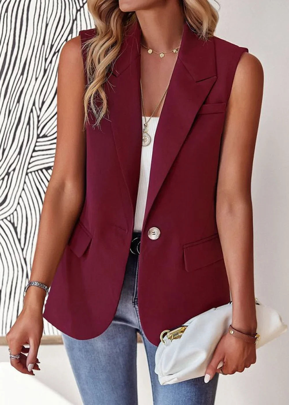 Maroon sleeveless blazer with a single button closure, worn by a model with light wash jeans and a white clutch.